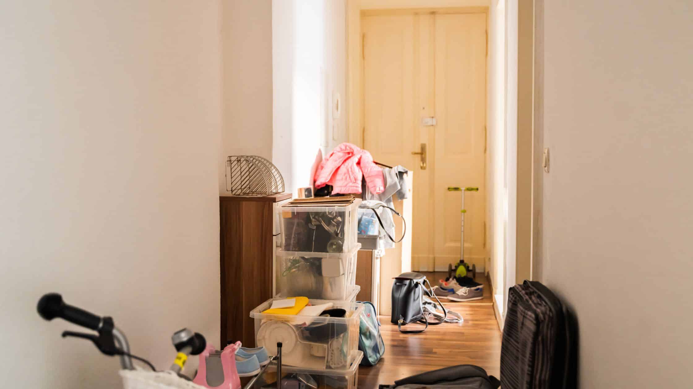 Cluttered hallway with plastic storage bins, scattered items, and personal belongings in need of a junk cleanout.