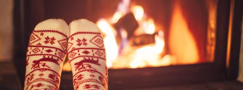 Cozy winter scene with feet in festive red and white socks warming by a crackling fireplace.